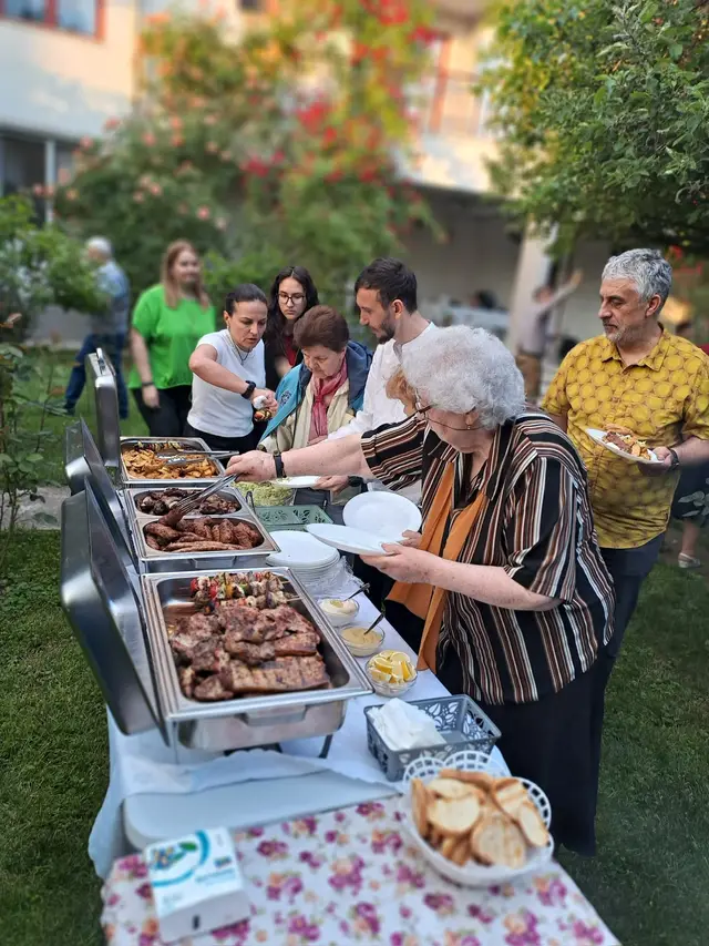 Invitati servindu-se de la gratarul cu mici si fripturi, la un eveniment in gradina