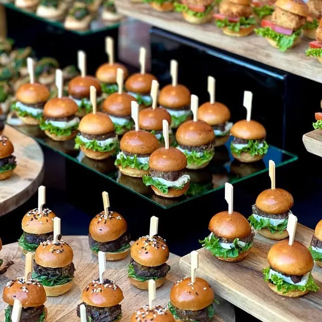 Mini burgeri asezati pe o etajera neagra, la un bufet de aperitive