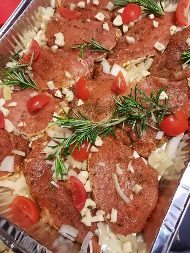 Cotlete marinate cu rozmarin, rosii si ceapa, pregatite in tava inainte de eveniment